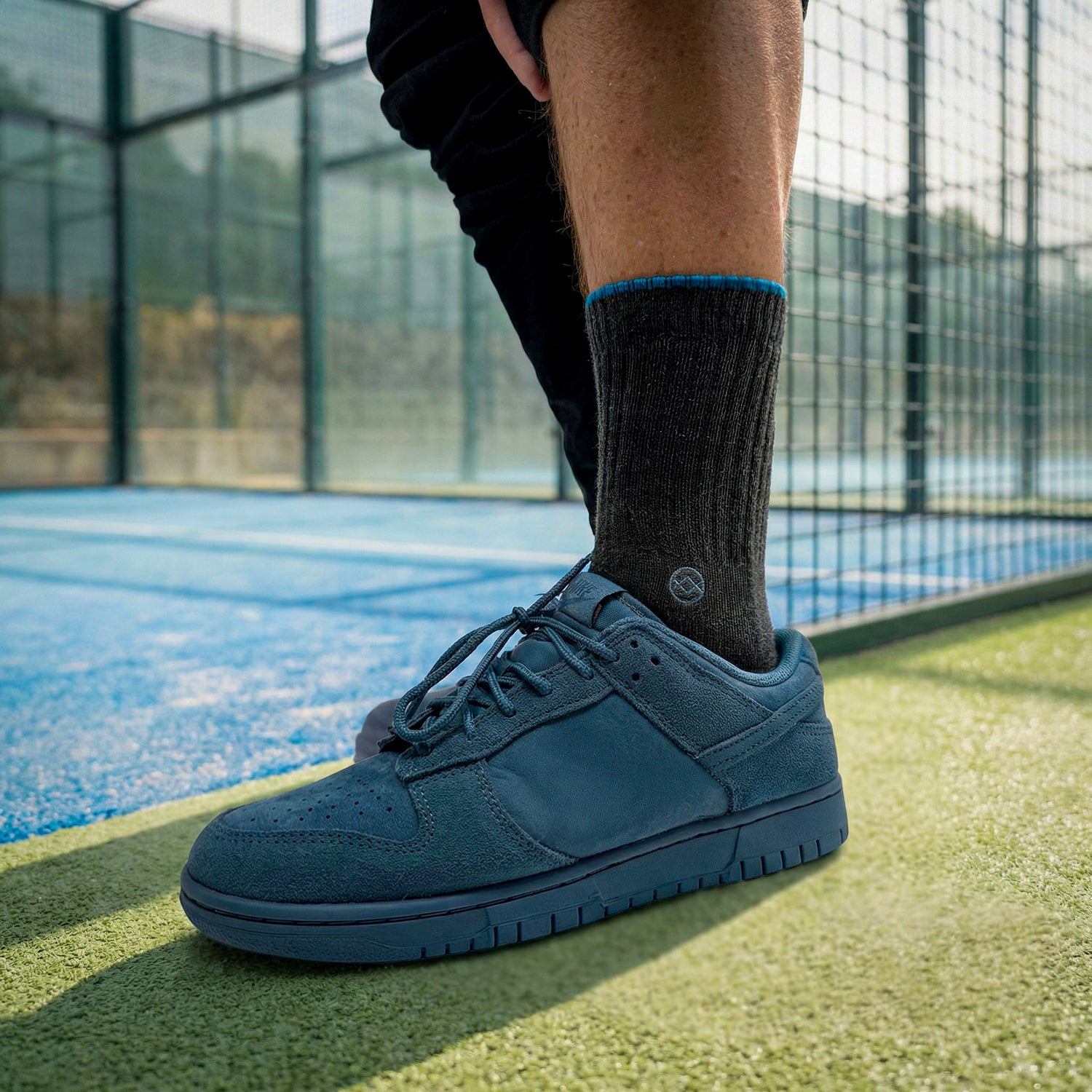 Dark grey WALK IT OFF merino wool socks (The 24/7 Antracite) worn with sneakers on a padel court.