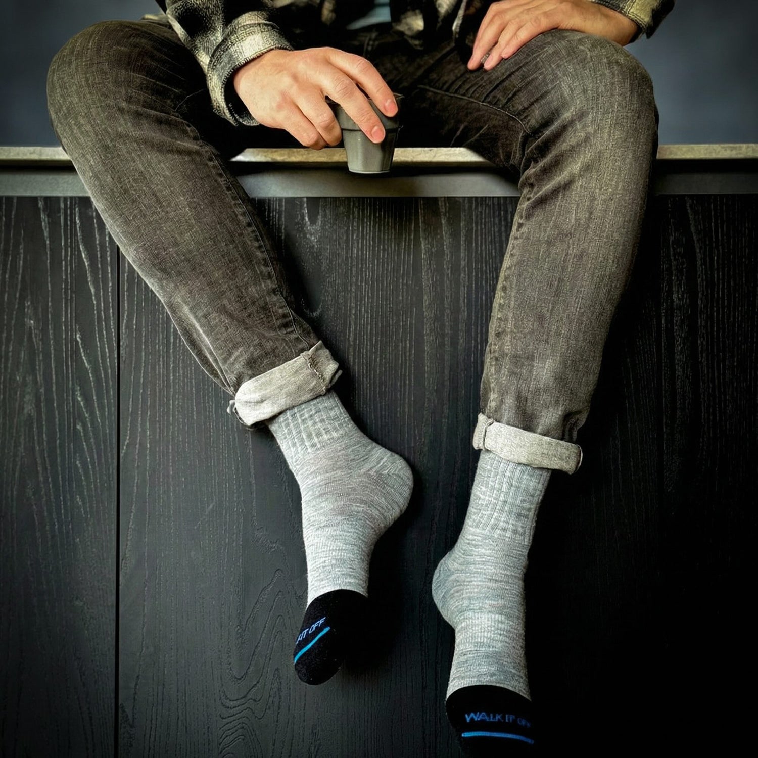 Man sitting on a kitchen counter wearing grey WALK IT OFF merino wool socks (The 24/7 Twister) while drinking coffee.