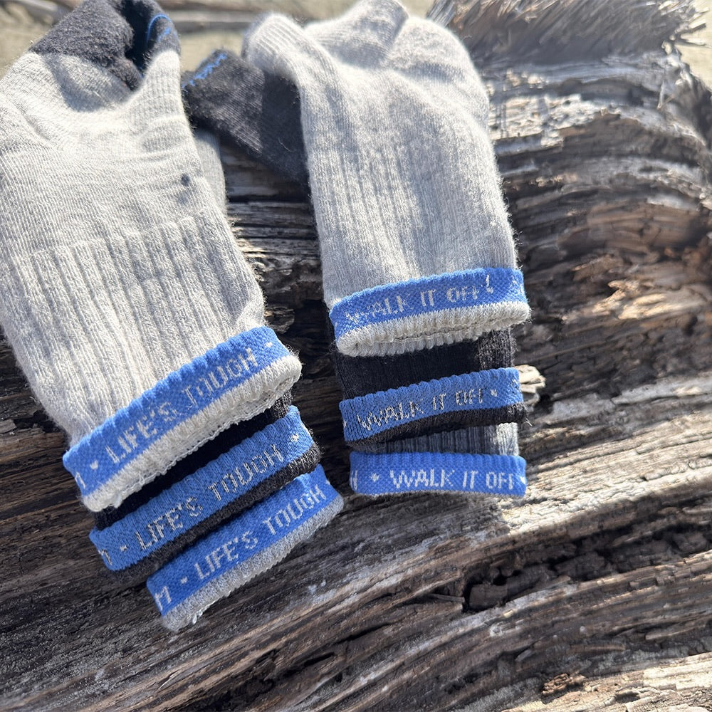 Close-up van gestapelde WALK IT OFF merino sokken met blauwe ‘Life’s Tough – Walk It Off’ branding.