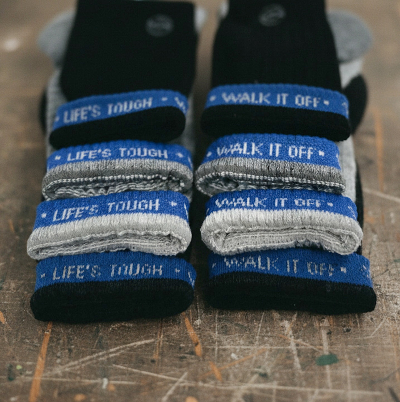 Gestapelde WALK IT OFF merino sokken in zwart en grijs, met blauwe details en Life’s Tough branding