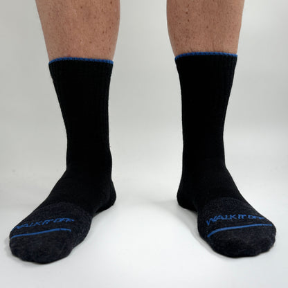 Model draagt de WALK IT OFF merino sokken in de kleur Black Magic, gefotografeerd recht van voren op een witte achtergrond.
