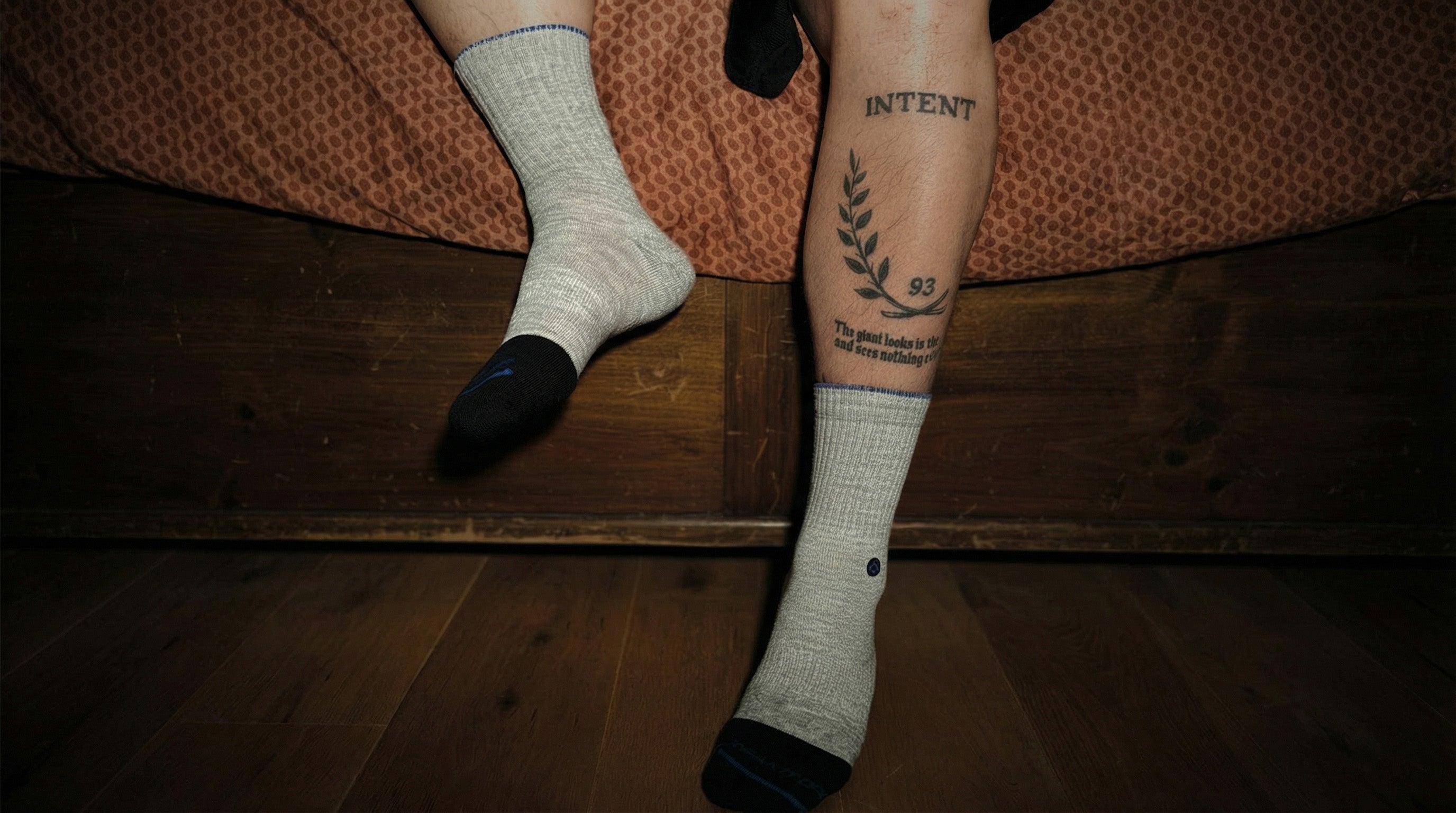 Persoon draagt WALK IT OFF merino sokken zittend op bed, lifestyle setting met houten vloer.