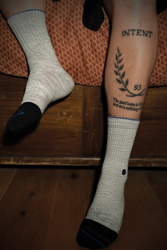 Persoon draagt WALK IT OFF merino sokken zittend op bed, lifestyle setting met houten vloer.